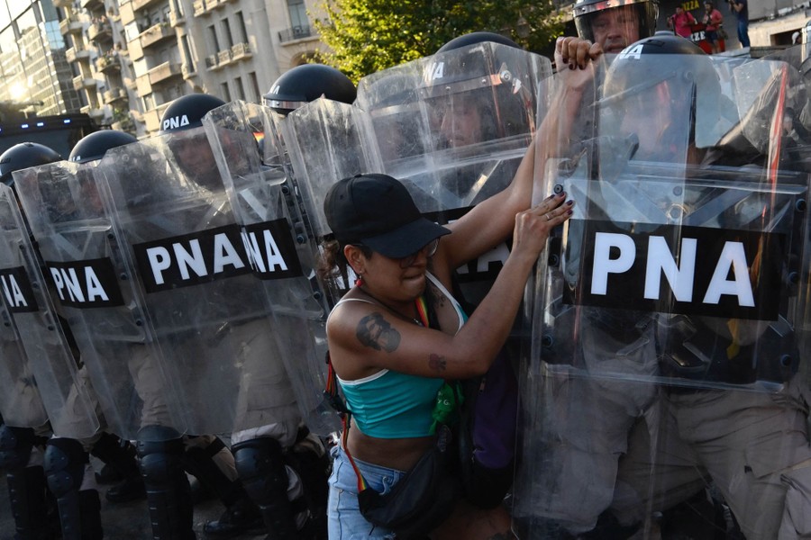 A person wrestles with a shield held by a riot police officer who is standing in a line with other officers.