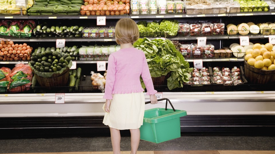 A young girl looks at the produce aisle in a grocery store.