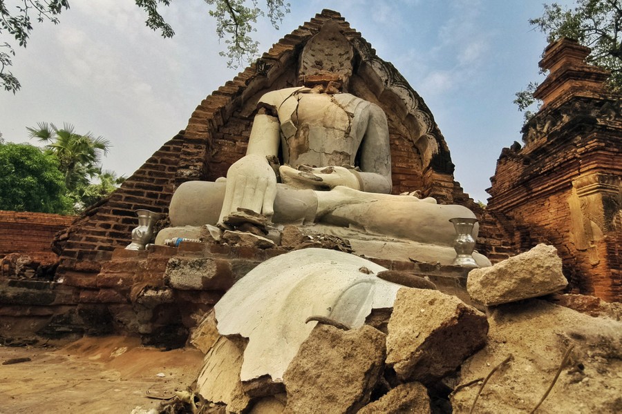 A quake-damaged Buddha statue, seen with parts of its broken face on the ground