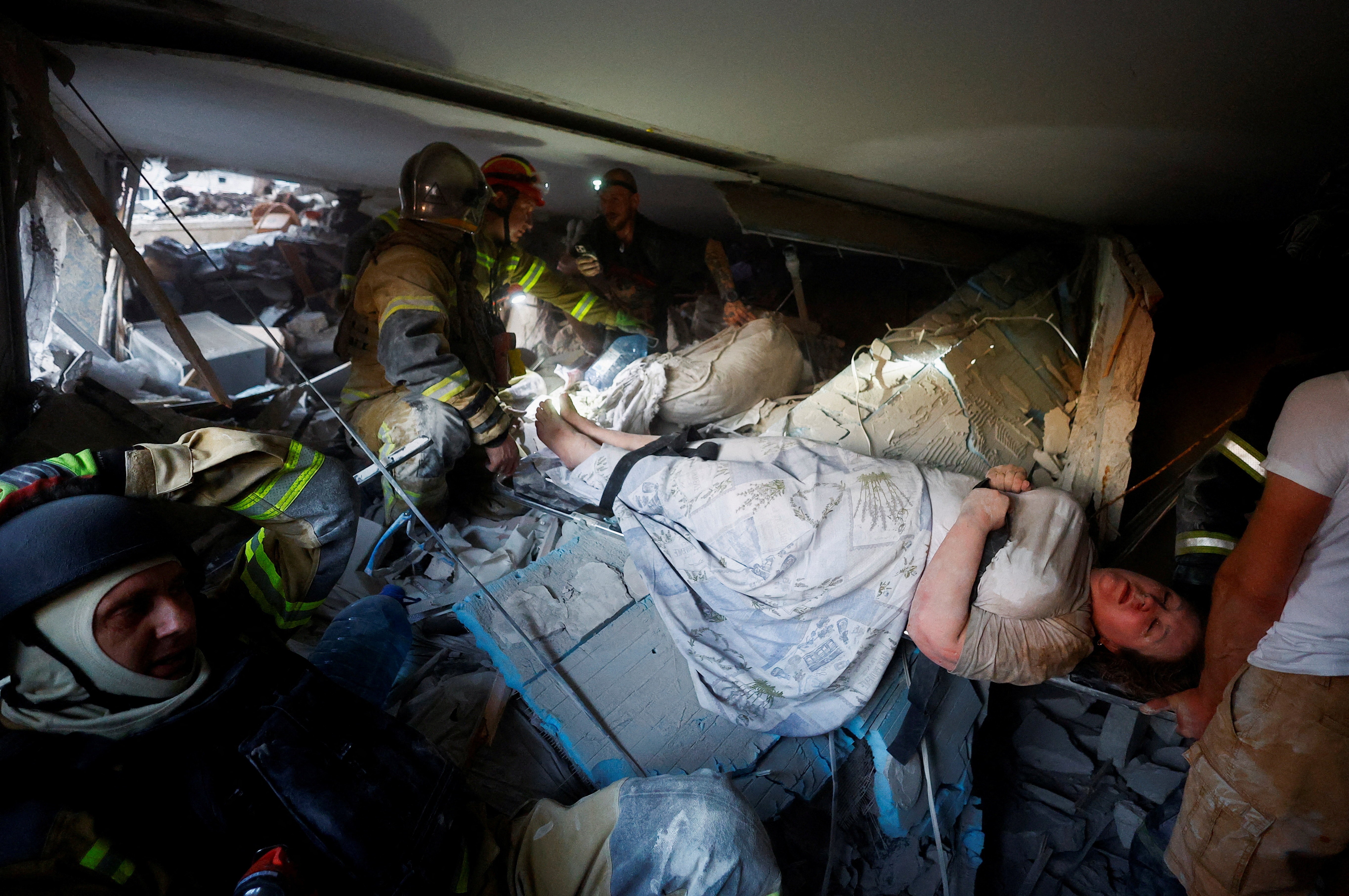Rescuers inside a cramped, partially collapsed apartment carry an injured woman on a stretcher.