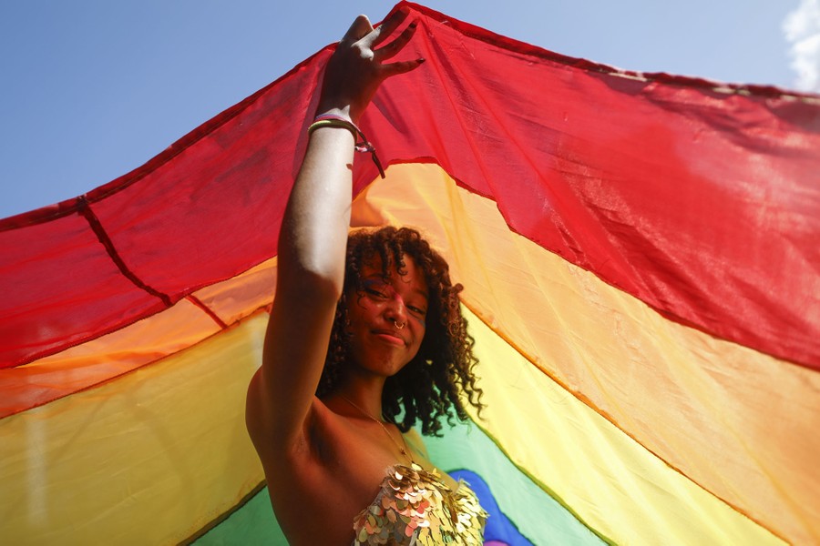 A person looks toward the camera while holding a large Pride flag above their head.