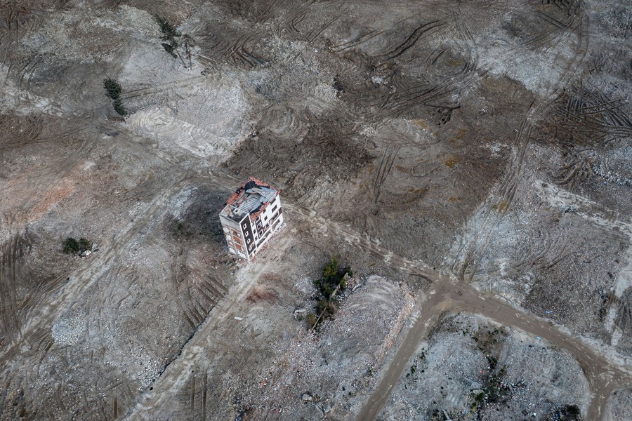 An aerial view of a lone damaged apartment block standing amid land cleared of earthquake debris
