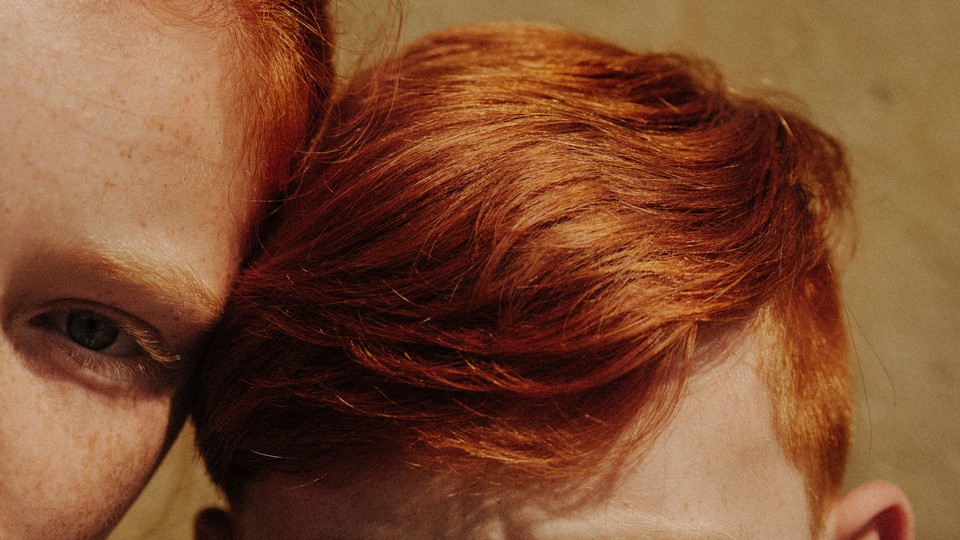 Two children with the same red hair color touching heads