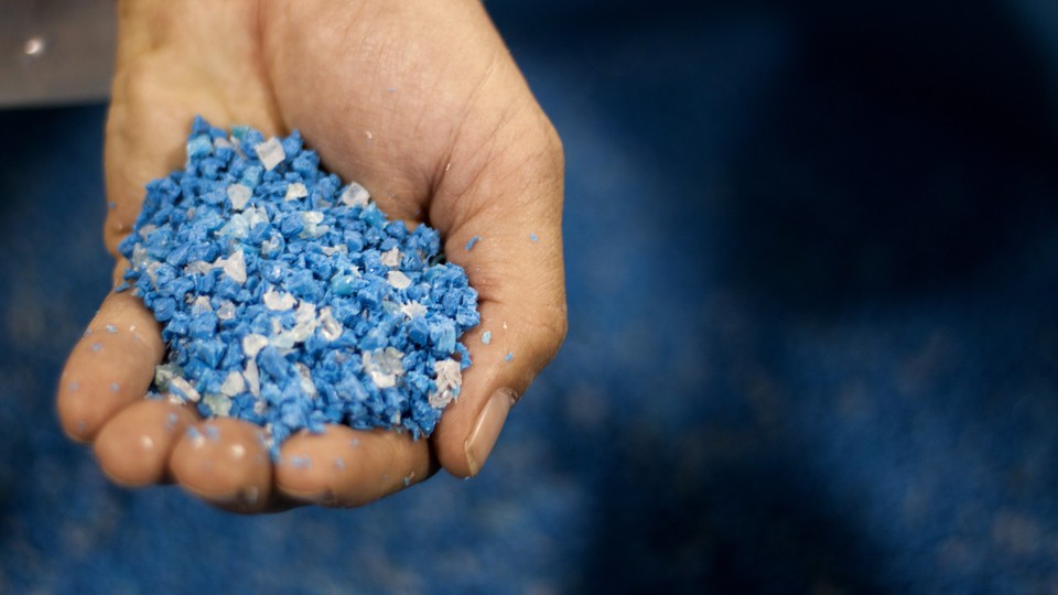 A hand holding a scoop of irregular blue plastic pellets, called nurdles