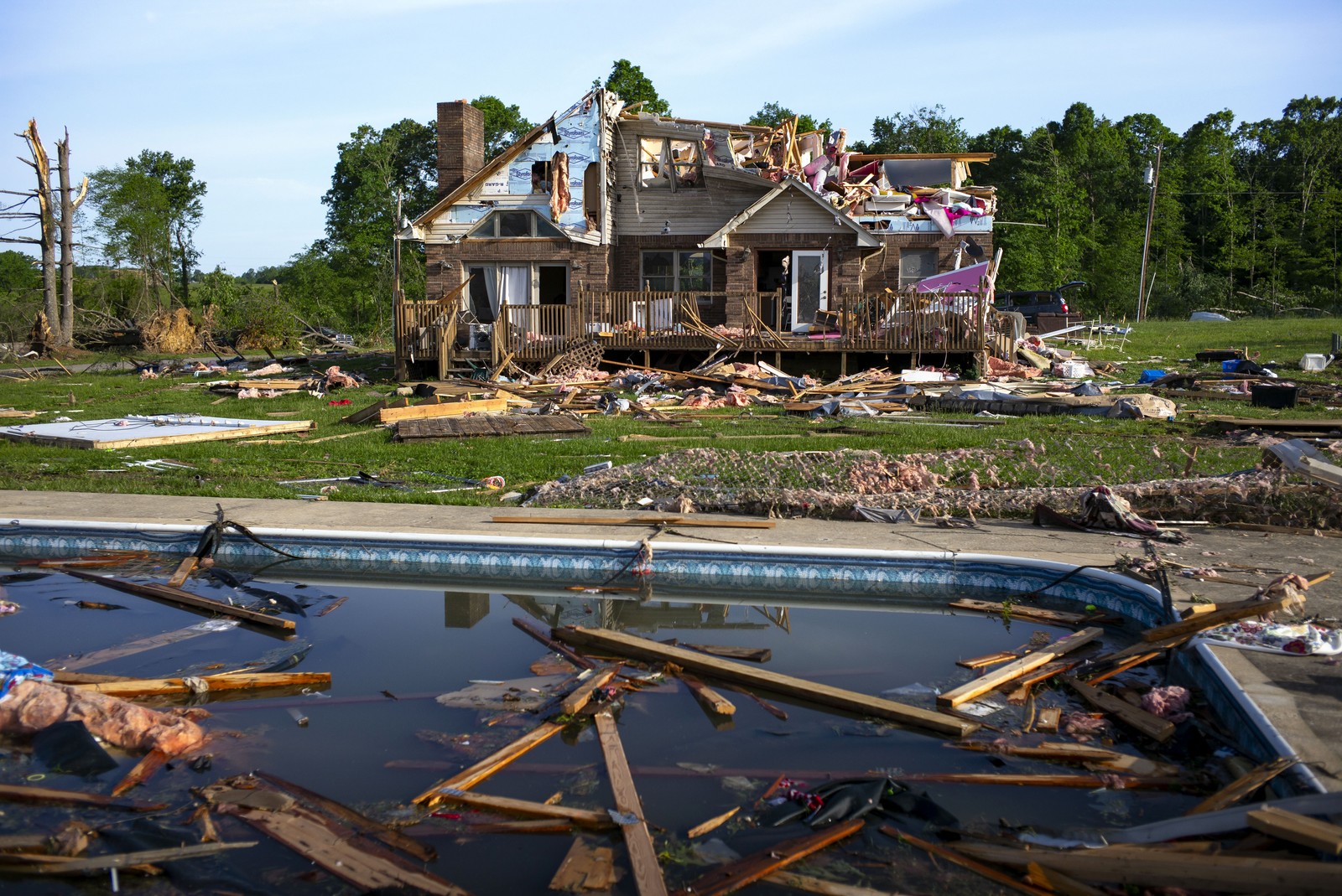 Debris floats in a pool near a severely storm-damaged house.