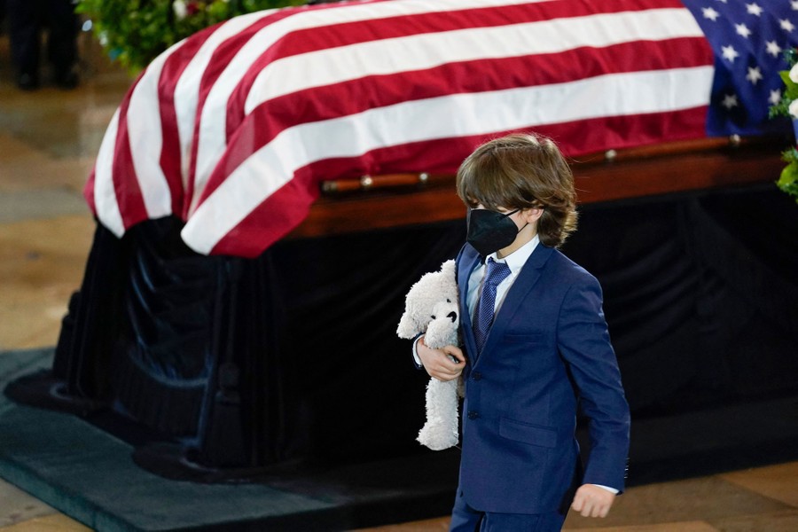 A boy carries a stuffed animal while walking past the casket of his father.