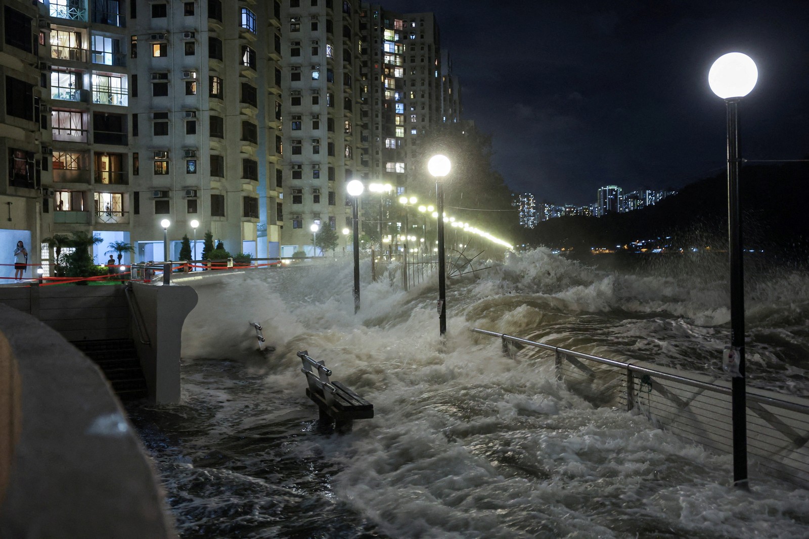 Strong waves crash over a seawall and splash a walkway and road in Hong Kong.