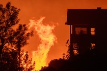 A fire approaches a house; the sky is orange.