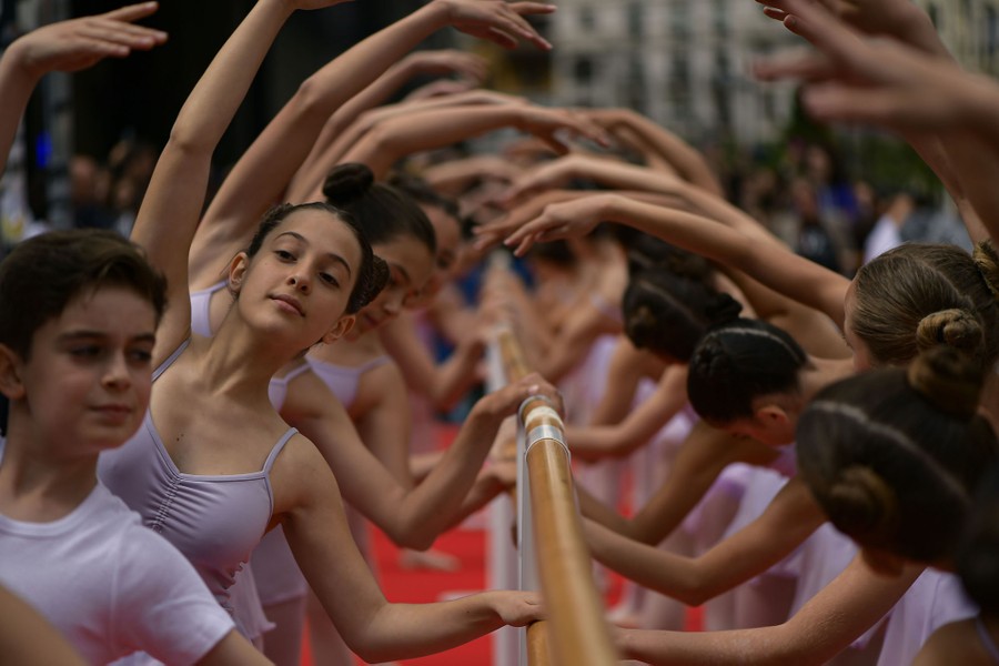 Two lines of young dancers pose while holding a barre.