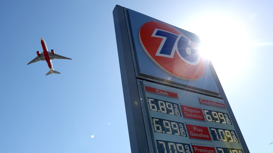 A plane in the sky next to a gas-station sign displaying gas prices