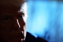 Trump's face, dimly lit and in front of a faded blue screen