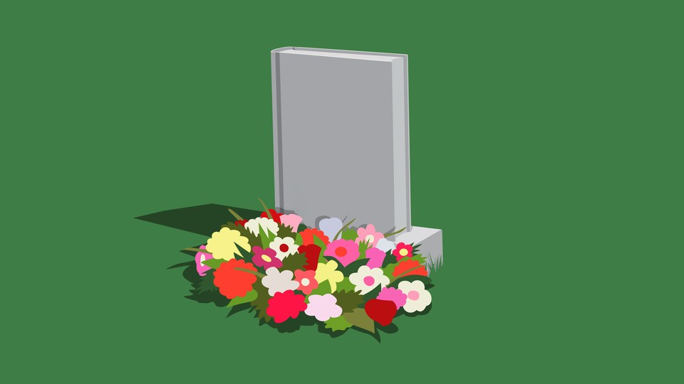 A gravestone that looks like a book with flowers at its base