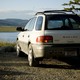 A white Subaru parked facing a body of water and mountains.