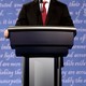 A politician's body at a lectern with words out of focus behind him.