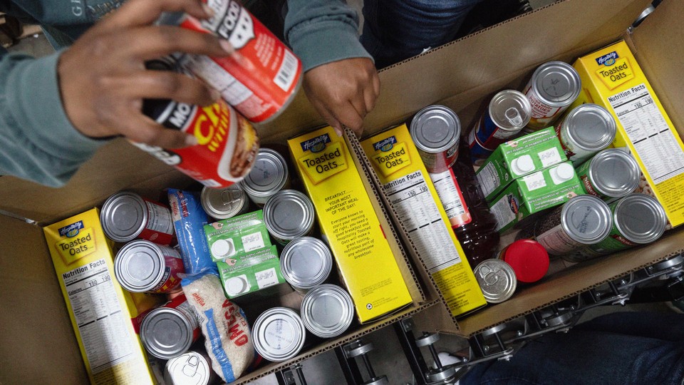 Photograph taken from above of two cardboard boxes being packed with non-perishable food items.