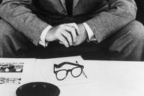 A man in a suit sits in front of papers.