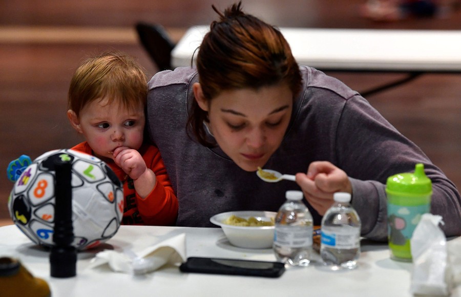 A woman has a spoonful of soup as her young son watches from her lap.