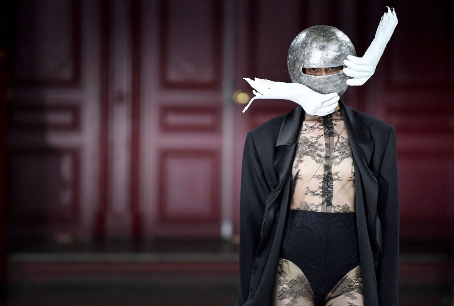 A model displays a garment with a silvery helmet that has plaster hands attached to it.