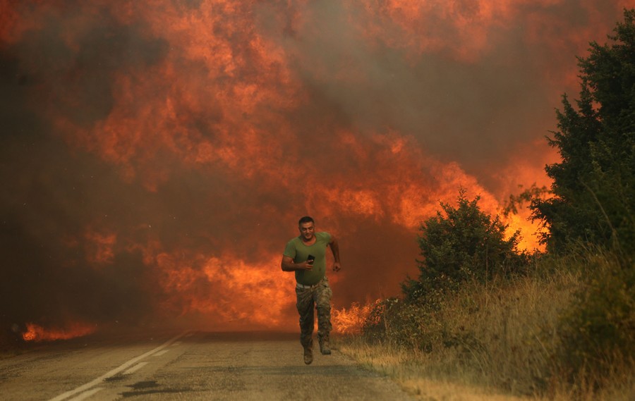 A man runs on a road in front of a wall of flame from a wildfire.