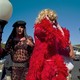 Three drag queens, one of whom is dressed in a long, red, feathered robe