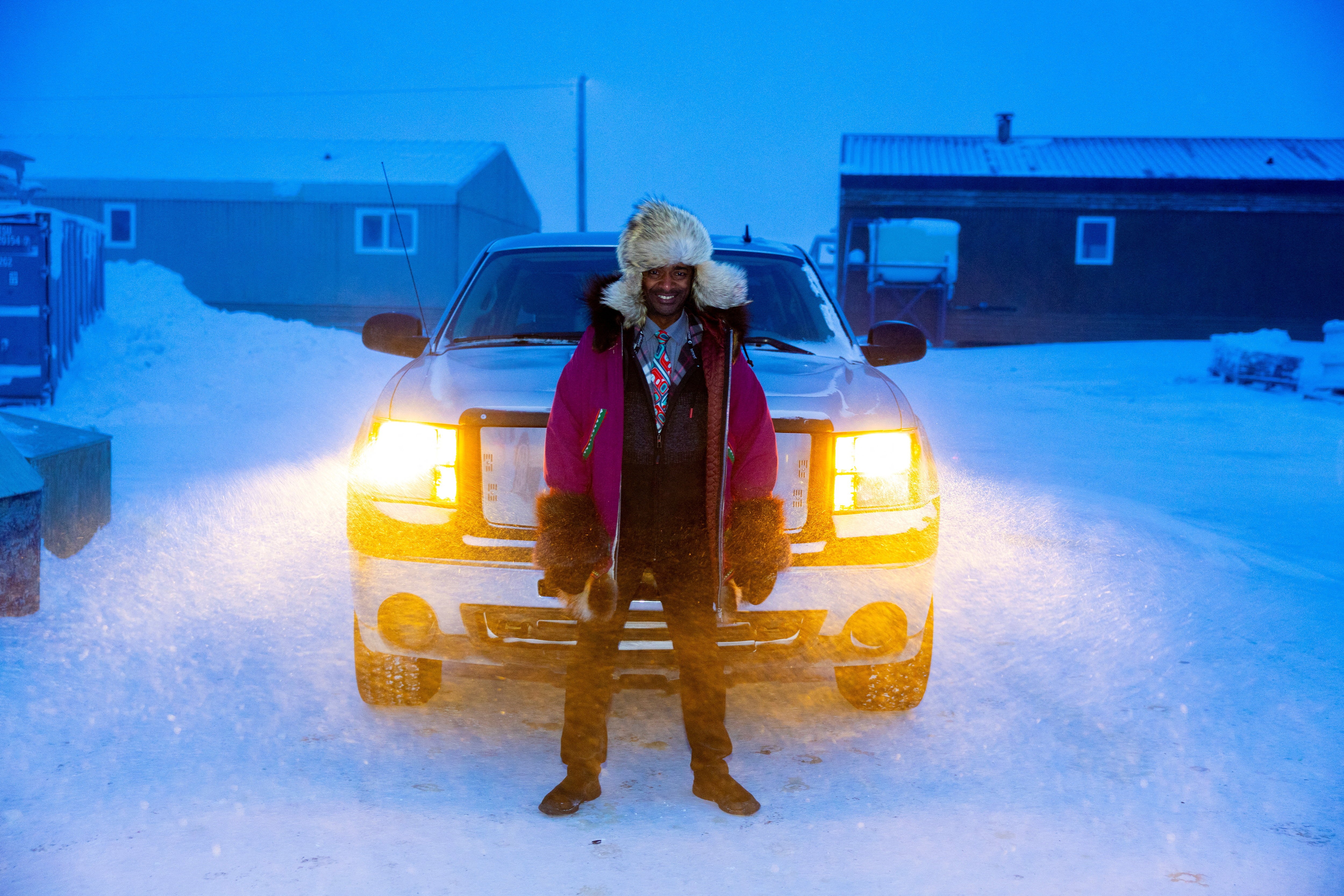 A person wearing cold-weather clothing poses, standing in front of a car.