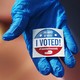 A gloved hand holding an "I Voted" sticker.