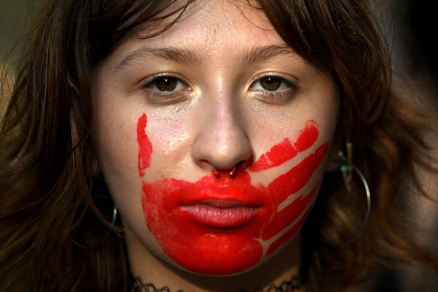 A close view of a woman with a red handprint painted across her mouth.