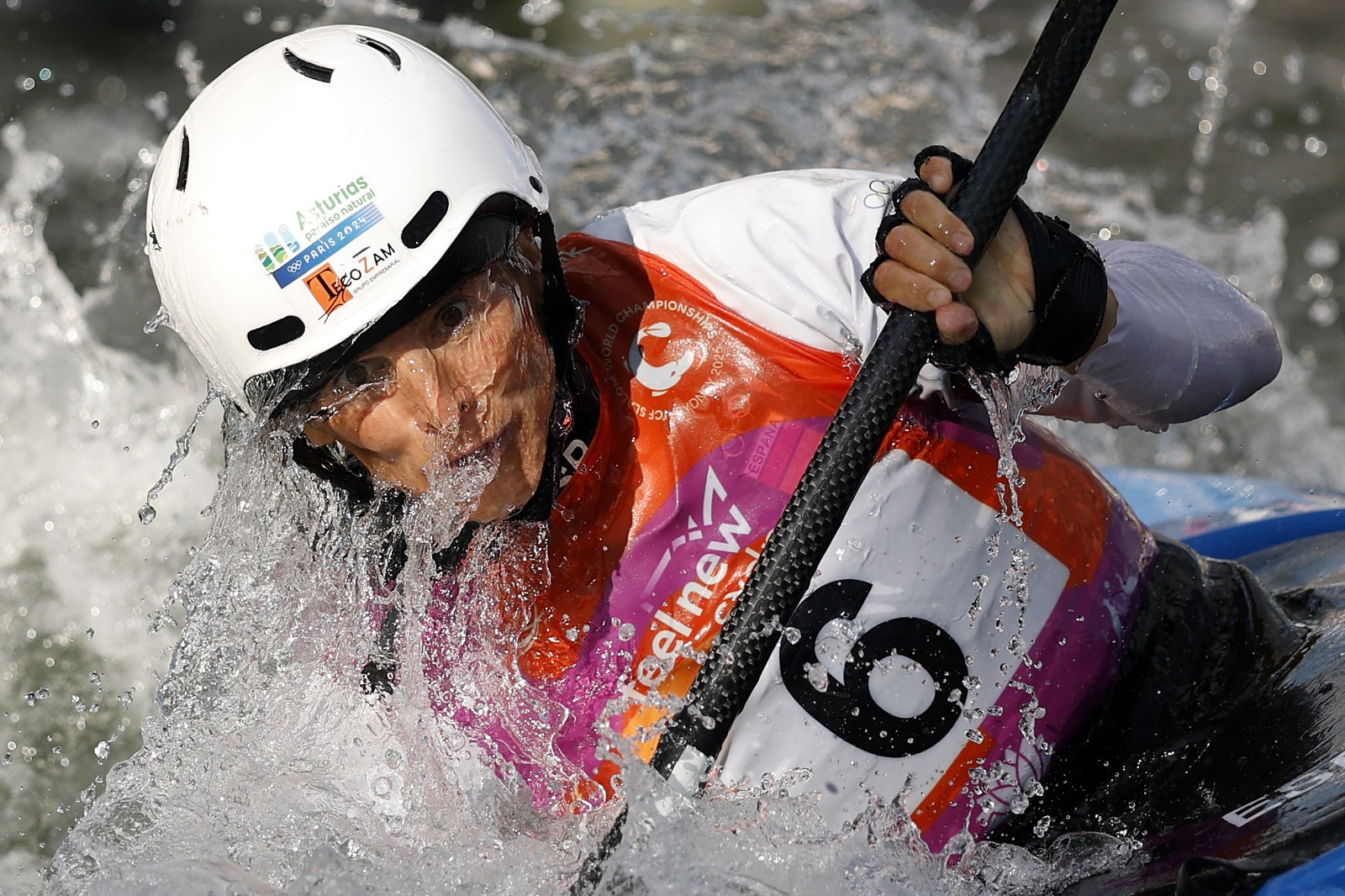 A competitive kayaker, seen during a race, with water flowing across their face and body.