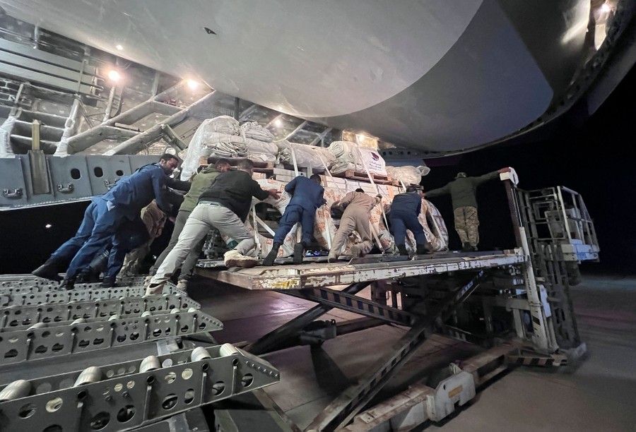 Workers unload relief items from a military cargo aircraft.