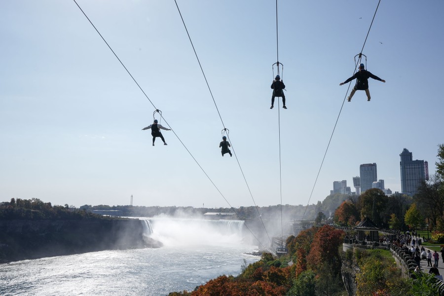 Four people ride zip lines toward a large waterfall.