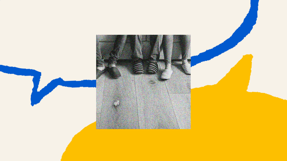 The outline of a blue speech bubble fills the top half of the screen. A yellow, filled-in speech bubble is on the bottom of the screen. In the middle is a black-and-white photo of three pairs of feet, photographed from the calf down in black and white. Each person is wearing a pair of house slippers, two with stripes, one is all black.