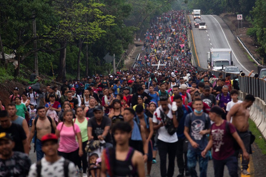 Hundreds of people are seen walking on a road beside a highway.