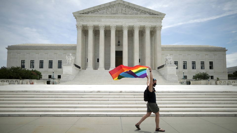 A person flies a pride rainbow flag outside the Supreme Court.
