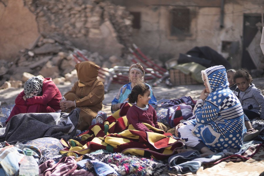 Families sit outside their destroyed homes, wrapped in blankets.