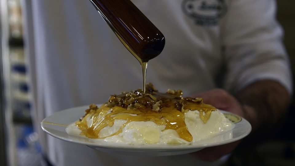 A person drizzling honey on a bowl of yogurt