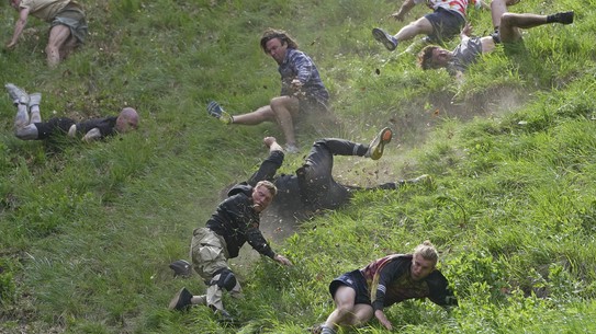 Eight men are seen tumbling and trying to run down a very steep hill.
