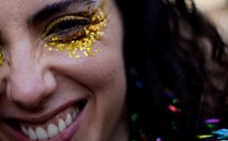 A close view of the face of a person wearing sparkly makeup around their eyes and smiling broadly