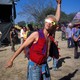 A man wearing eclipse glasses and colorful clothing gestures upward.