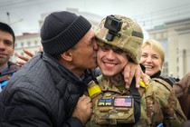 A civilian kisses a smiling soldier as others look on.