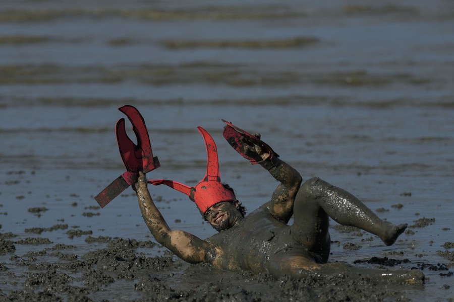 A festival-goer wearing parts of a costume rolls about in dark mud.