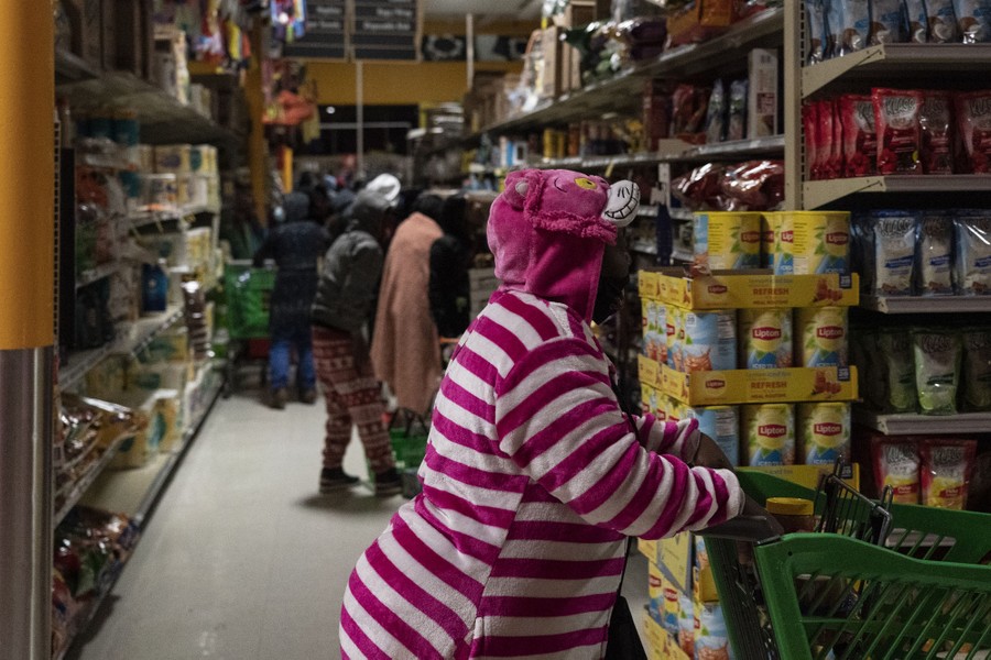 Several people shop in a grocery store under dim lighting.