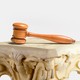 A gavel atop a Greek-looking column