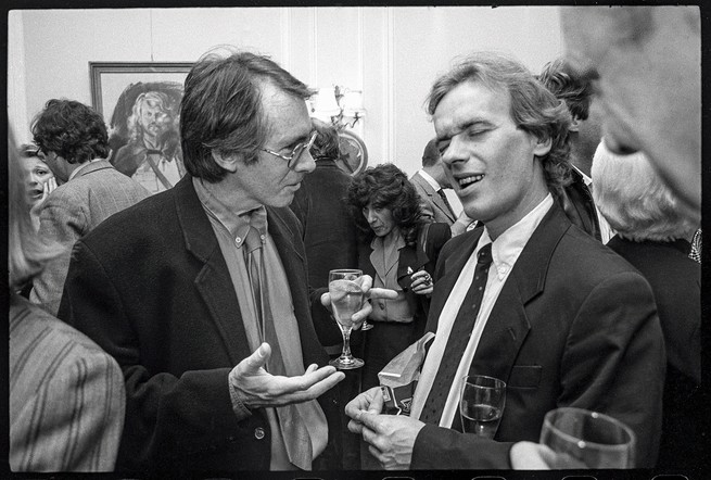 photo of two men in ties and suit jackets talking and holding drinks in crowded room, McEwan gesturing with hands and Amis reacting with eyes closed