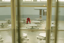 a color photographs of a man wearing a prison jumpsuit sitting alone in a lunch room