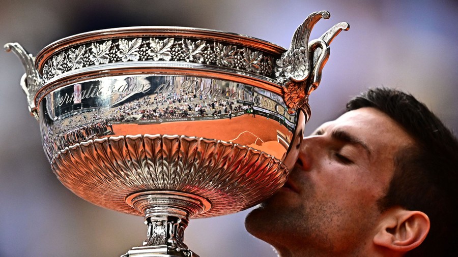 A tennis player holds up and kisses a large silver trophy.
