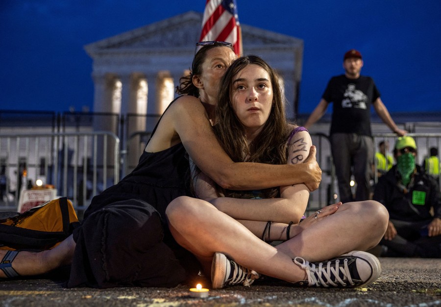 A woman holds her daughter while both sit on the ground in front of the United States Supreme Court.