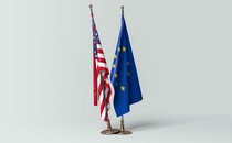 The U.S. flag standing next to the EU flag; the former's base rests atop the latter's.