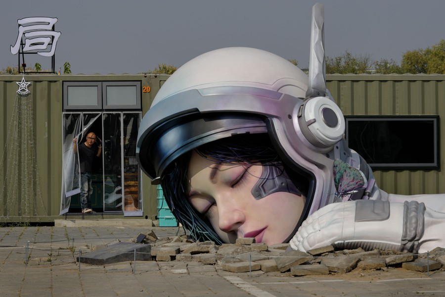 A person looks out of a restaurant door at a large sculpture of the head of an astronaut appearing to emerge from the ground.