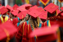 The backs of graduates in red caps and gowns