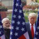 Color photo of Narendra Modi standing next to Donald Trump with three American flags in the foreground